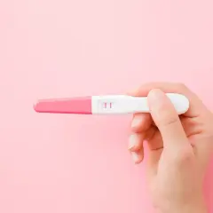 Dłoń trzyma test ciążowy z dwoma kreskami. To może oznaczać, że faza lutealna zakończyła się sukcesem.