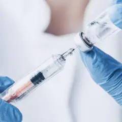 Ręce w niebieskich rękawiczkach przygotowują zastrzyk. W fiolce znajduje się płyn, który zostanie pobrany do strzykawki. To może być szczepionka przeciwko dur brzuszny.