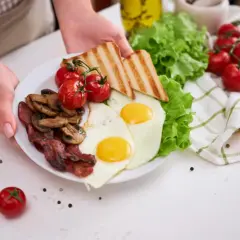 Pyszne śniadanie: jajka sadzone, chrupiący bekon, pieczarki, pomidorki, tosty i sałata. Idealne, by zacząć dzień!