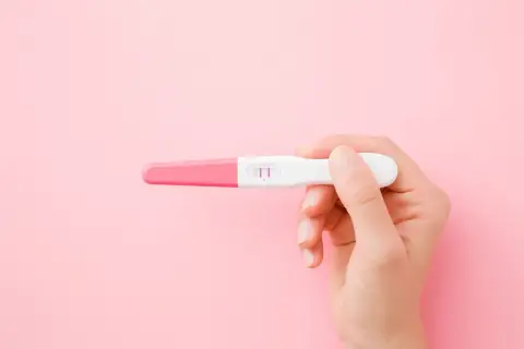 Dłoń trzyma test ciążowy z dwoma kreskami. To może oznaczać, że faza lutealna zakończyła się sukcesem.