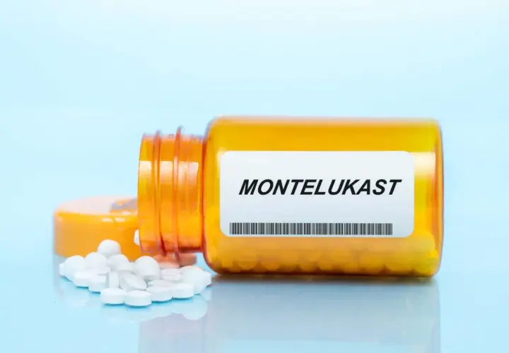 Pomarańczowa butelka z tabletkami montelukast, kilka białych tabletek rozsypanych obok.