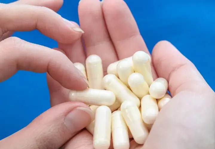 Dłonie trzymają garść białych kapsułek, które mogą zawierać biotynę, wspierającą zdrowie włosów i paznokci.