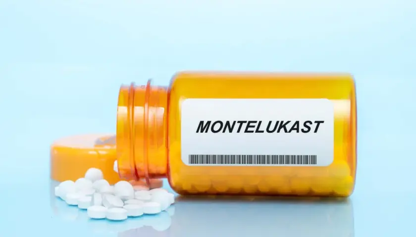 Pomarańczowa butelka z tabletkami montelukast, kilka białych tabletek rozsypanych obok.