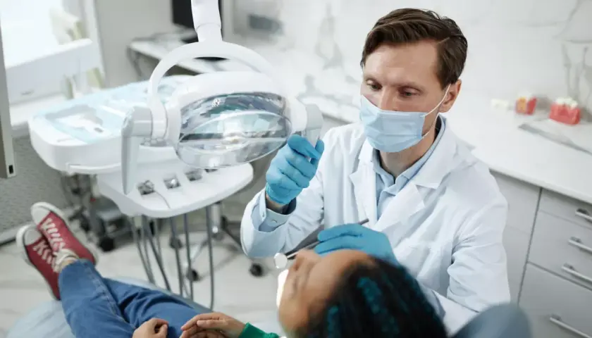 Dentysta w masce i rękawiczkach bada pacjenta w gabinecie stomatologicznym.