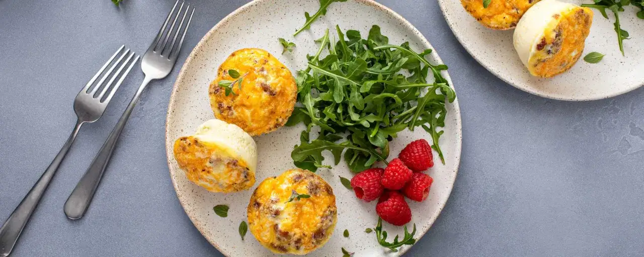 Pyszne muffinki jajeczne z serem i kiełbasą, podane z rukolą i malinami. Idealne, by zjeść na śniadanie.